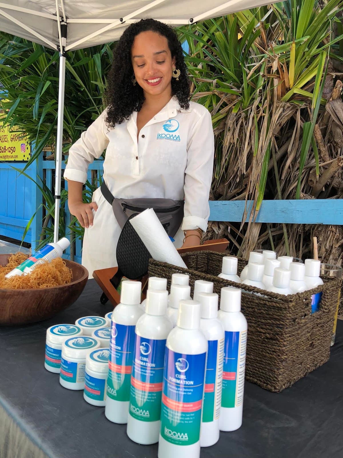 A woman in a white shirt showcases skincare products at a market stall.