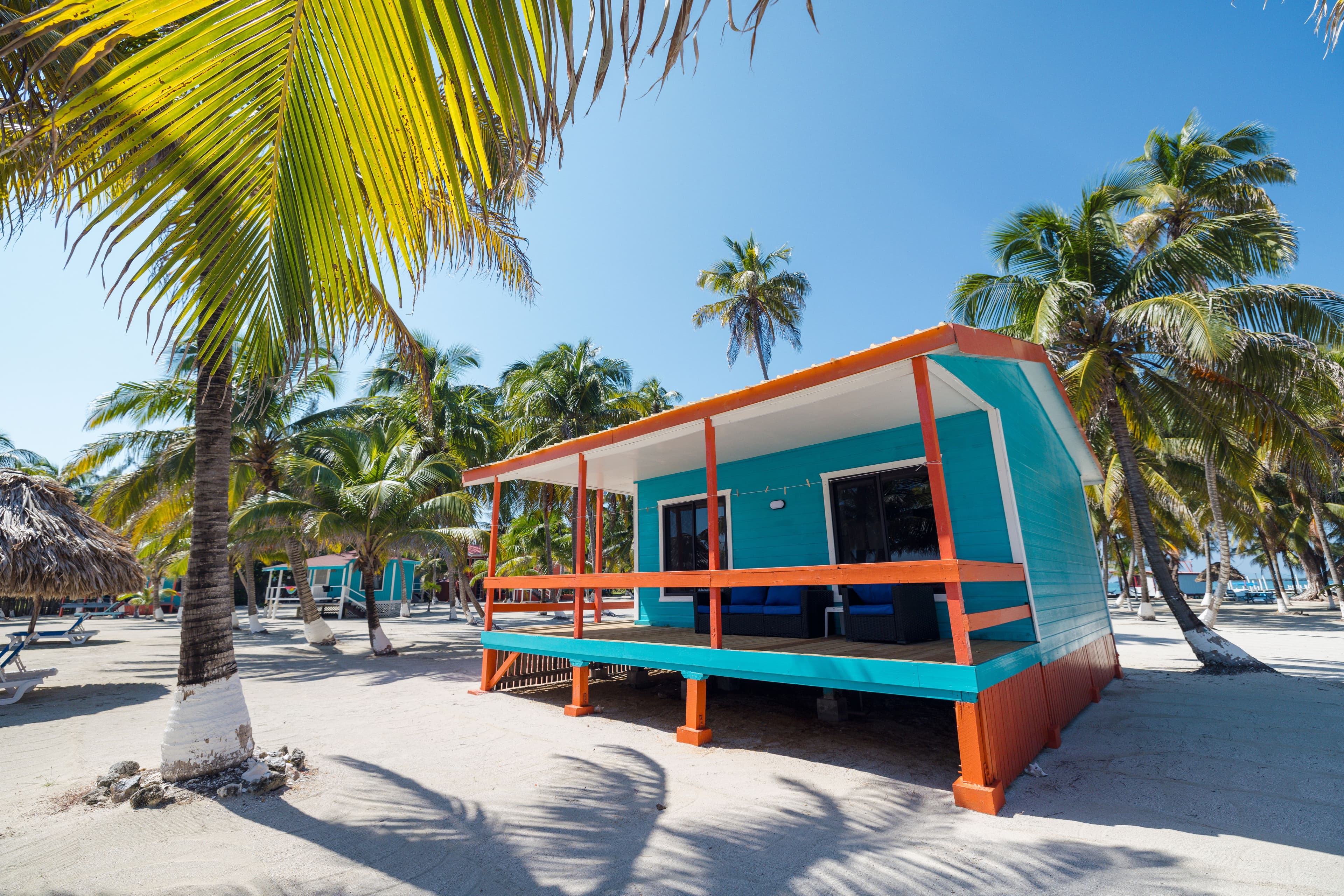 A colorful beach house surrounded by palm trees on a sandy shore.