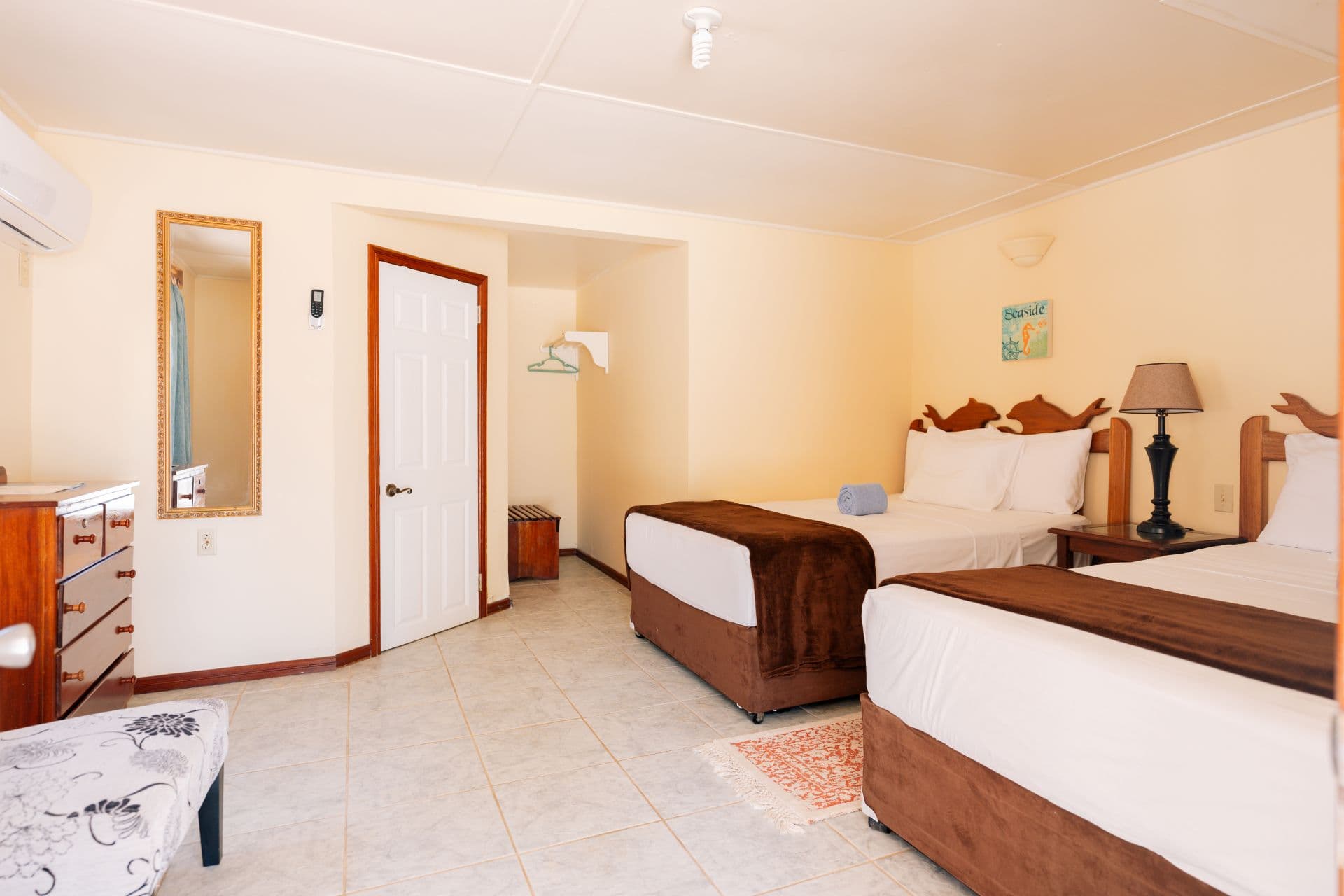 A cozy hotel room with two beds, a dresser, and a mirror in a light-colored interior.
