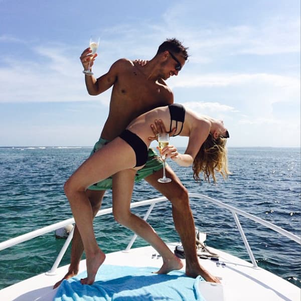 A man and woman dance joyfully on a boat, holding glasses while overlooking the ocean.