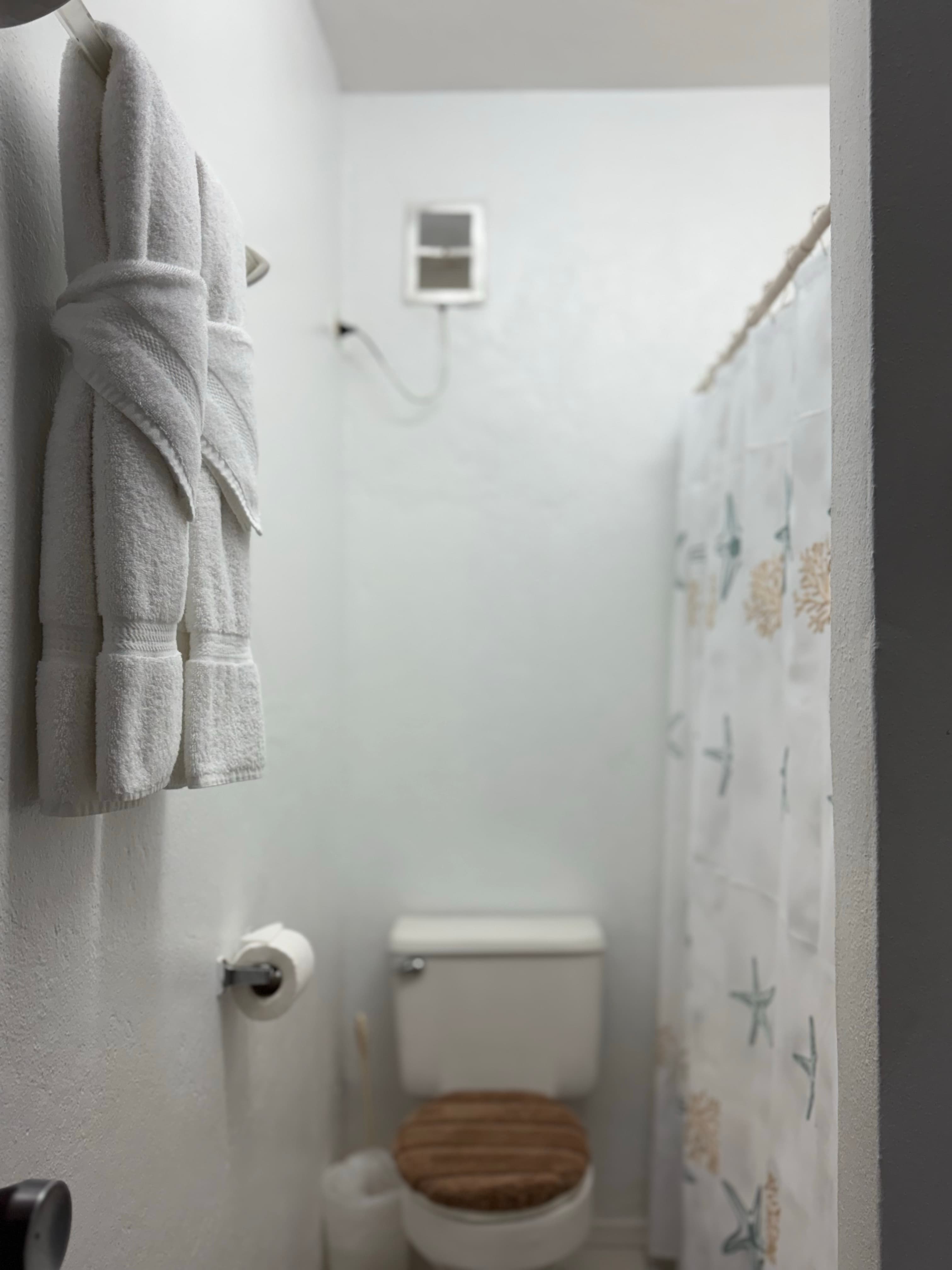 A small bathroom with white walls featuring neatly hung towels, a toilet, and a shower with a patterned curtain.