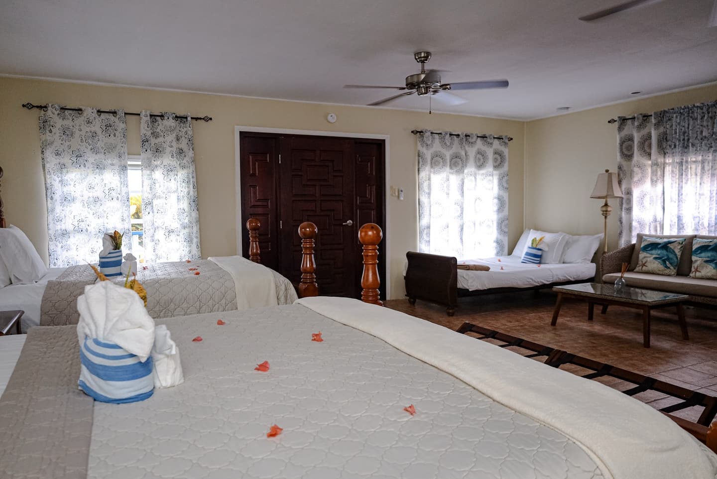 A cozy hotel room featuring two beds, a sofa, decorative curtains, and a ceiling fan.