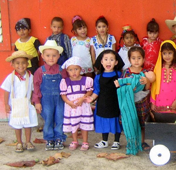 A group of children in traditional clothing pose together in front of a bright orange wall. A group of children in traditional clothing pose together in front of a bright orange wall.