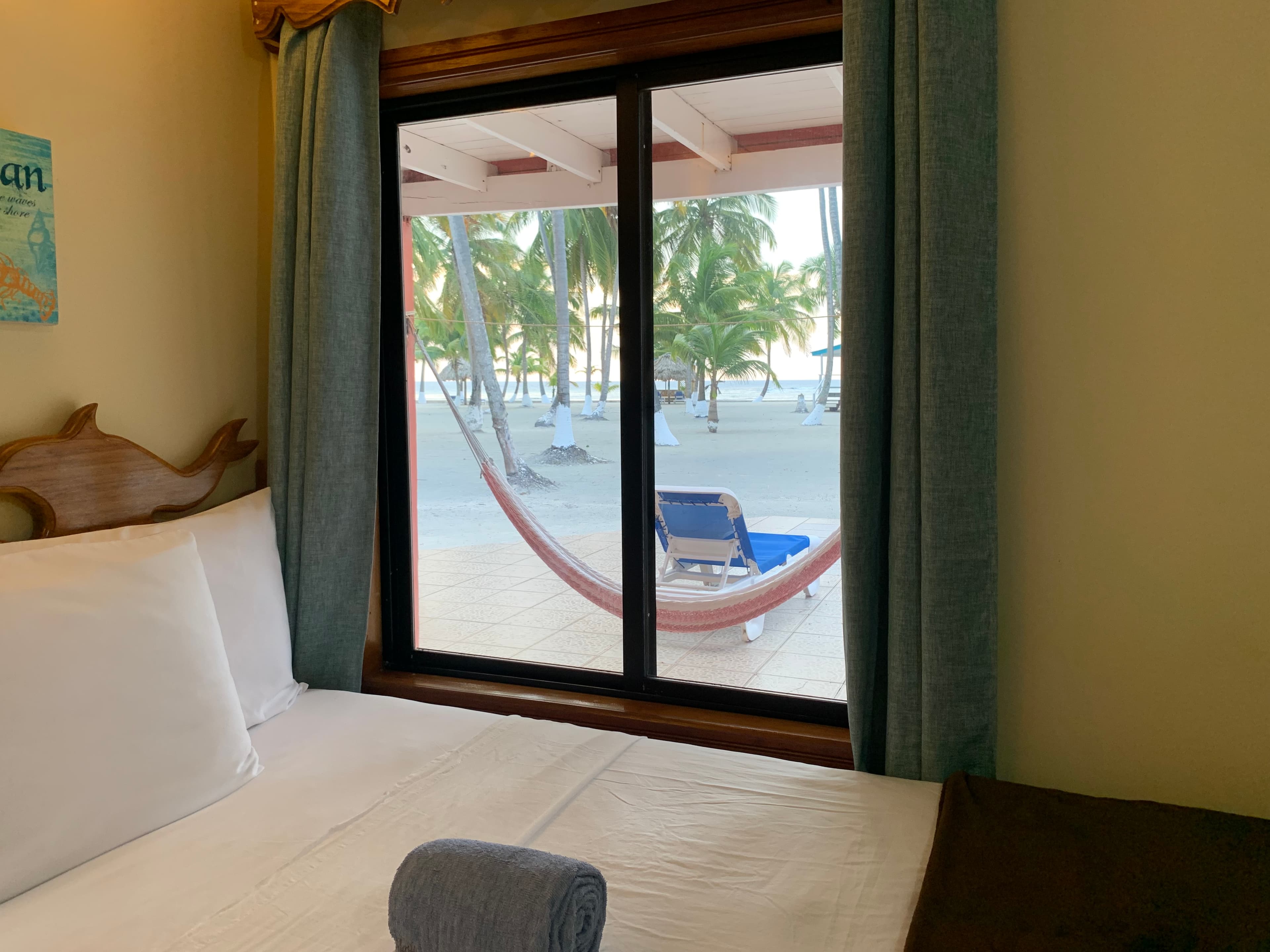 A cozy bedroom with a view of a hammock and palm trees outside a window.