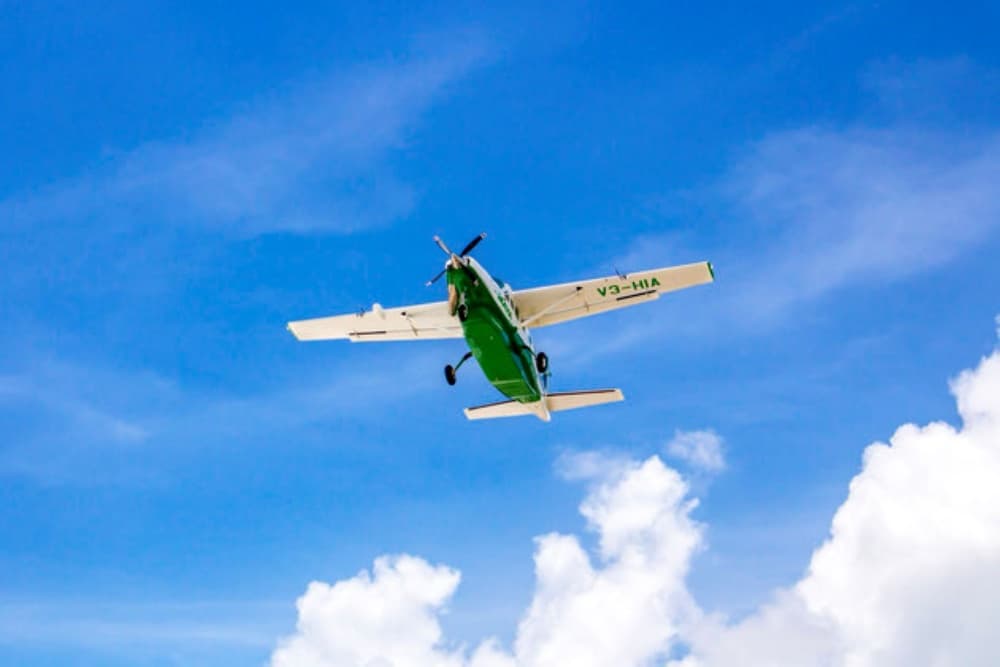 A green and white airplane flies through a clear blue sky with fluffy clouds.