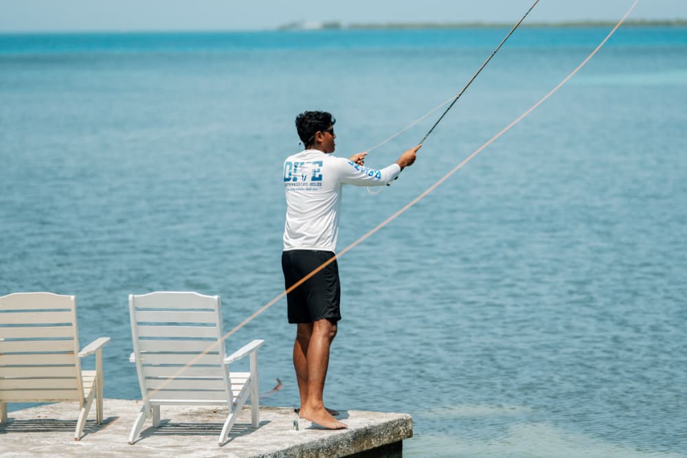 A person stands on a dock, casting a fishing line into the water.