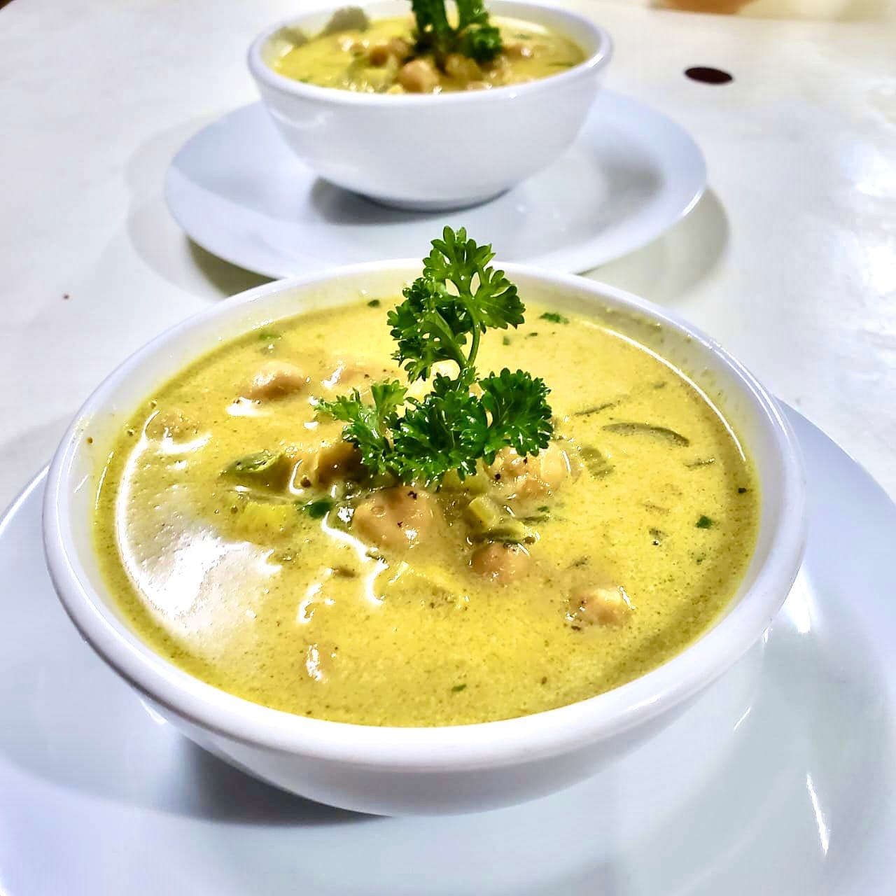 A close-up of a bowl of creamy soup garnished with parsley, with a second bowl blurred in the background.