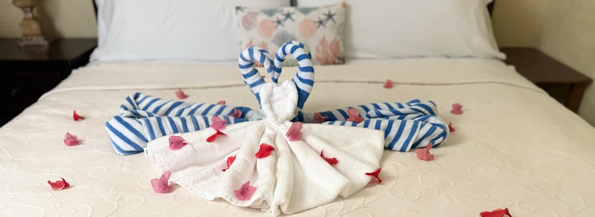 A beautifully arranged towel sculpture resembling a swan, adorned with flower petals, on a neatly made bed.