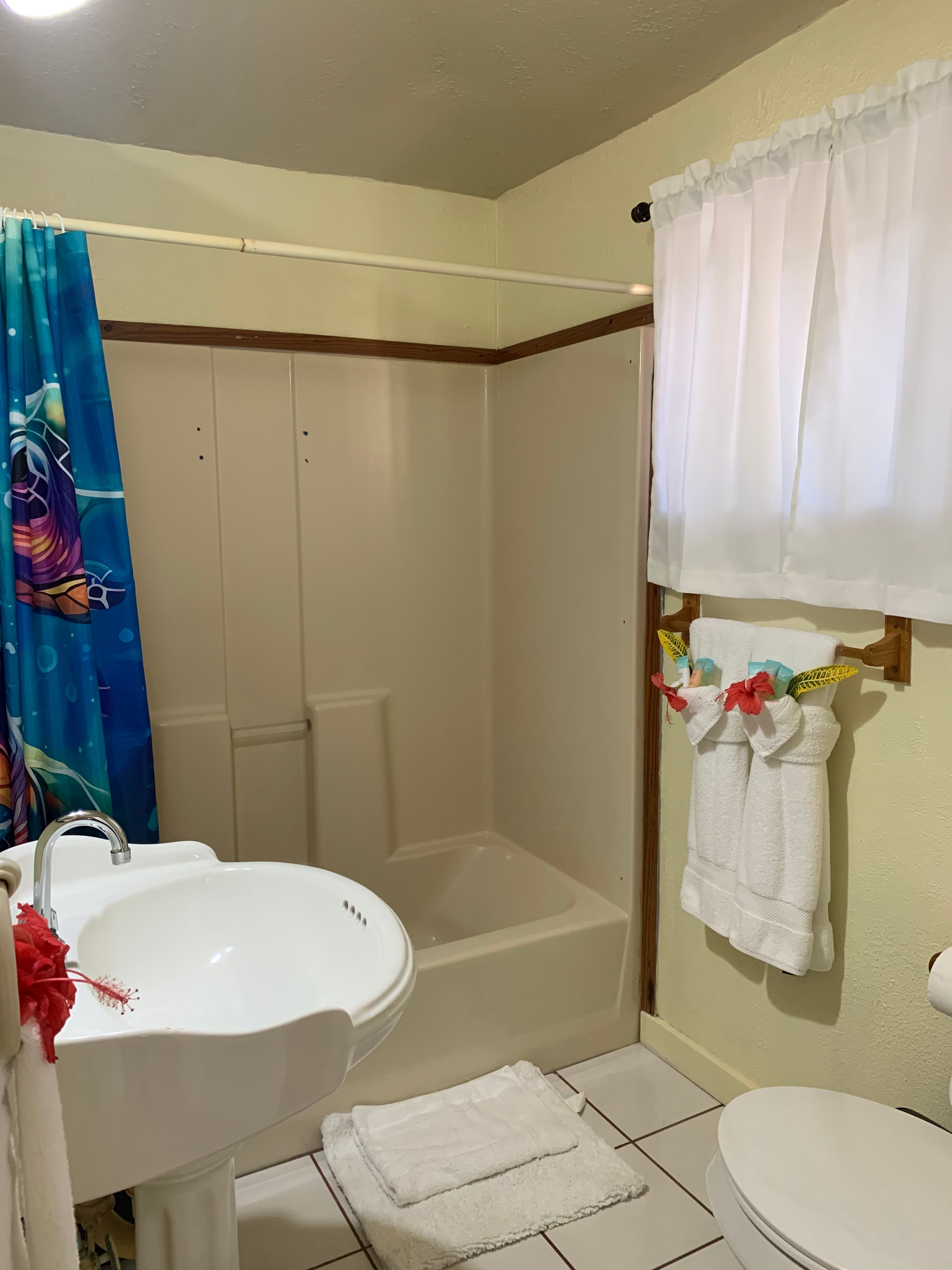 A compact bathroom featuring a shower with a colorful curtain, a sink, a toilet, and neatly arranged towels.