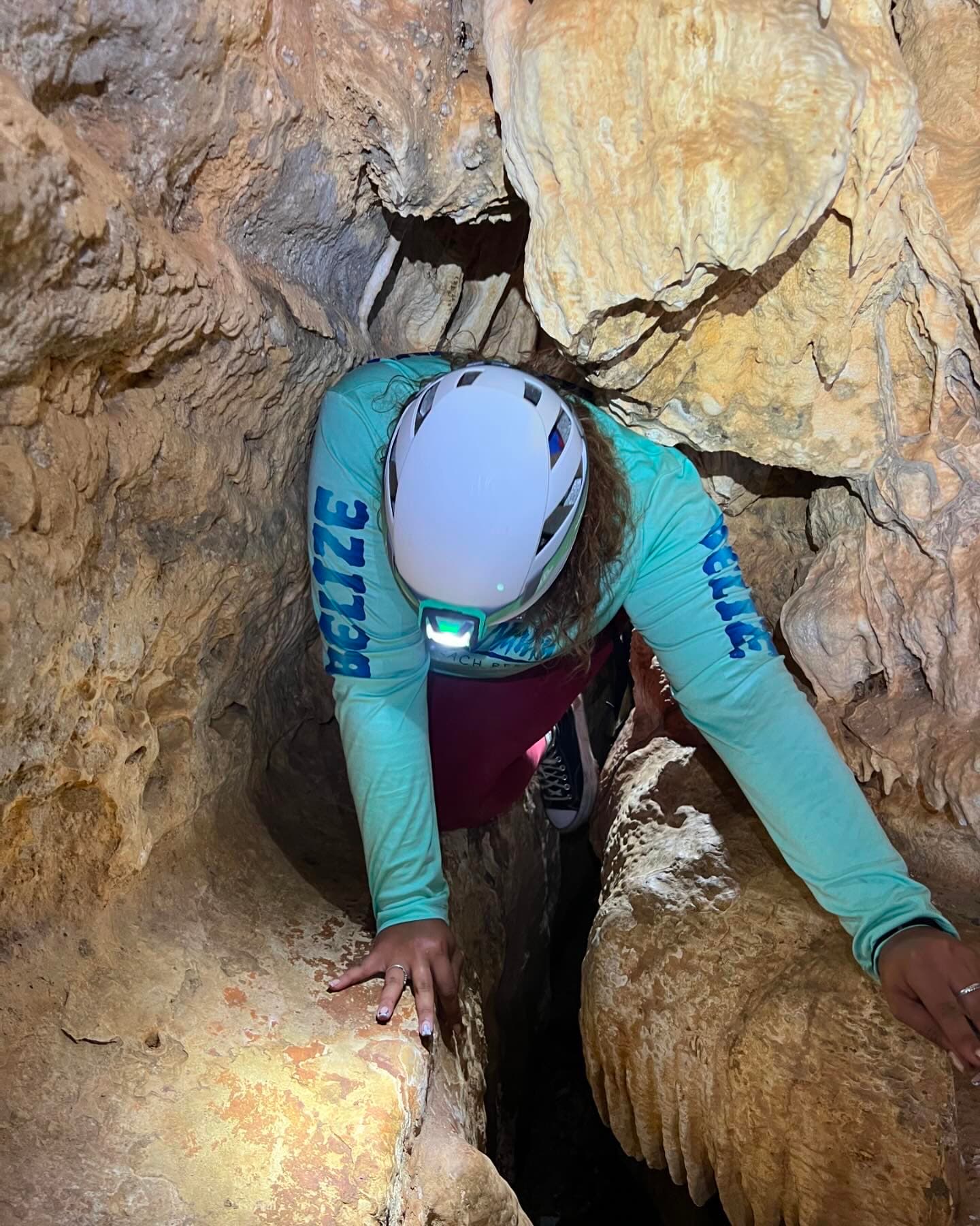 A person in a helmet crawls through a narrow rock passage, using their hands for support.