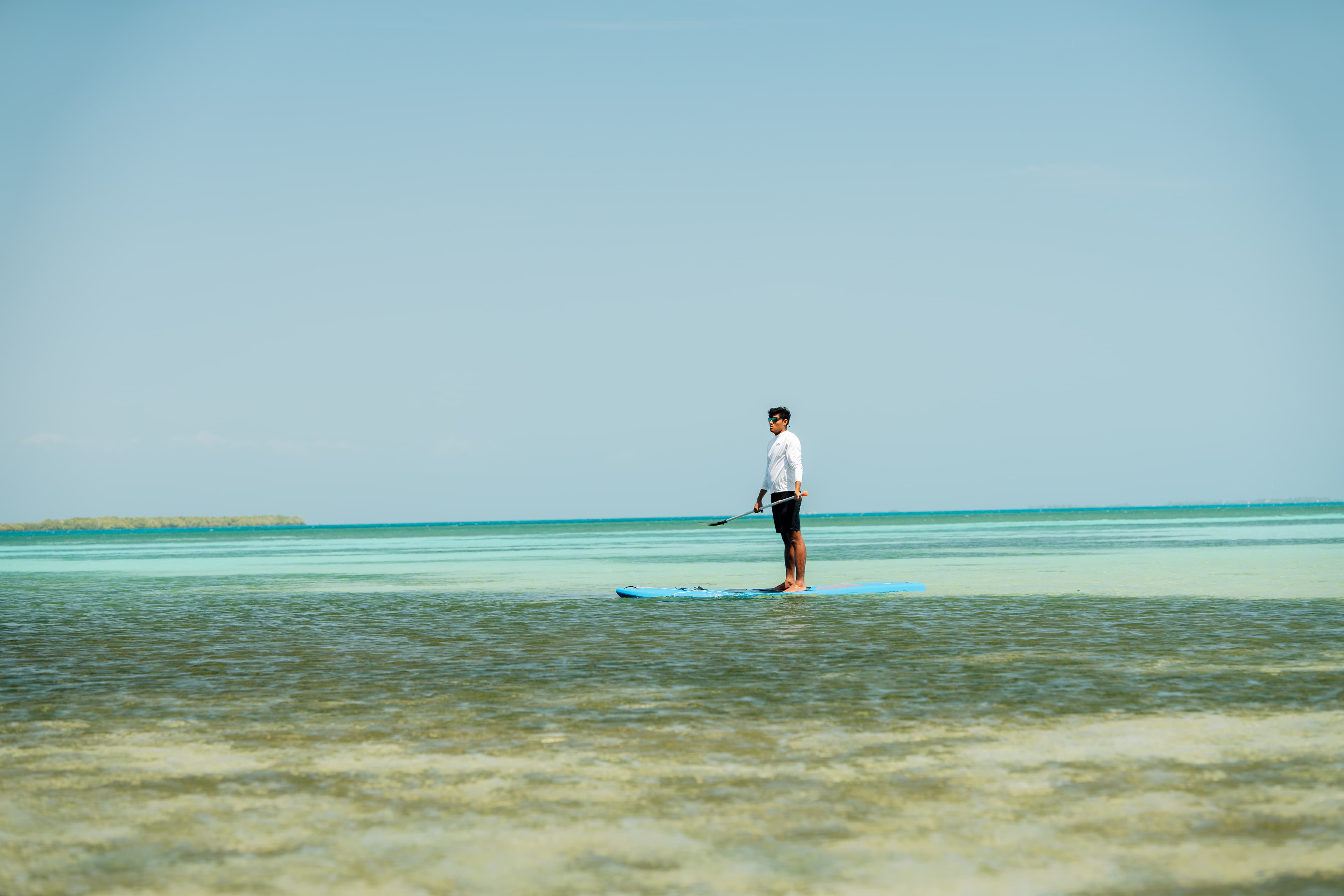 A person stands on a paddleboard in a calm, shallow sea.