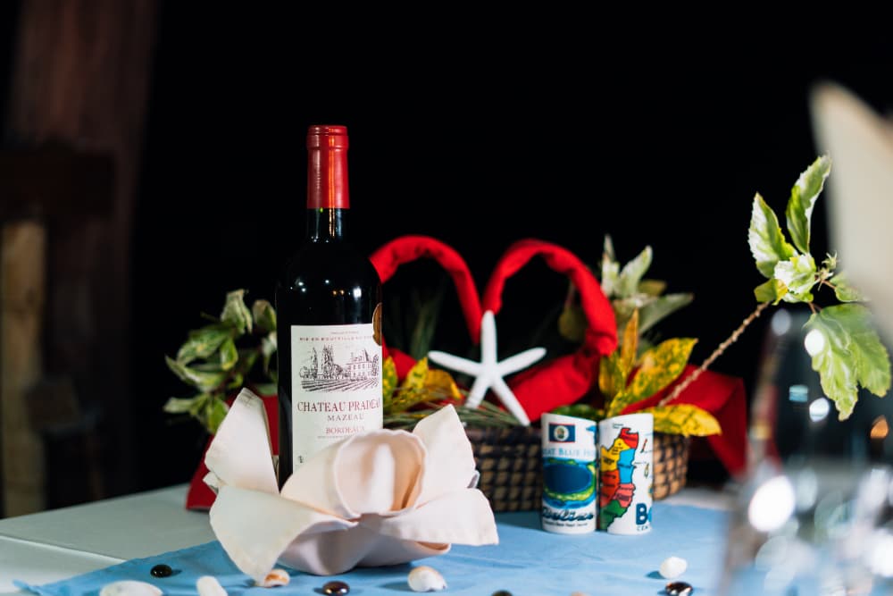 A bottle of red wine is surrounded by decorative elements including leaves, napkins, and colorful shot glasses on a table.