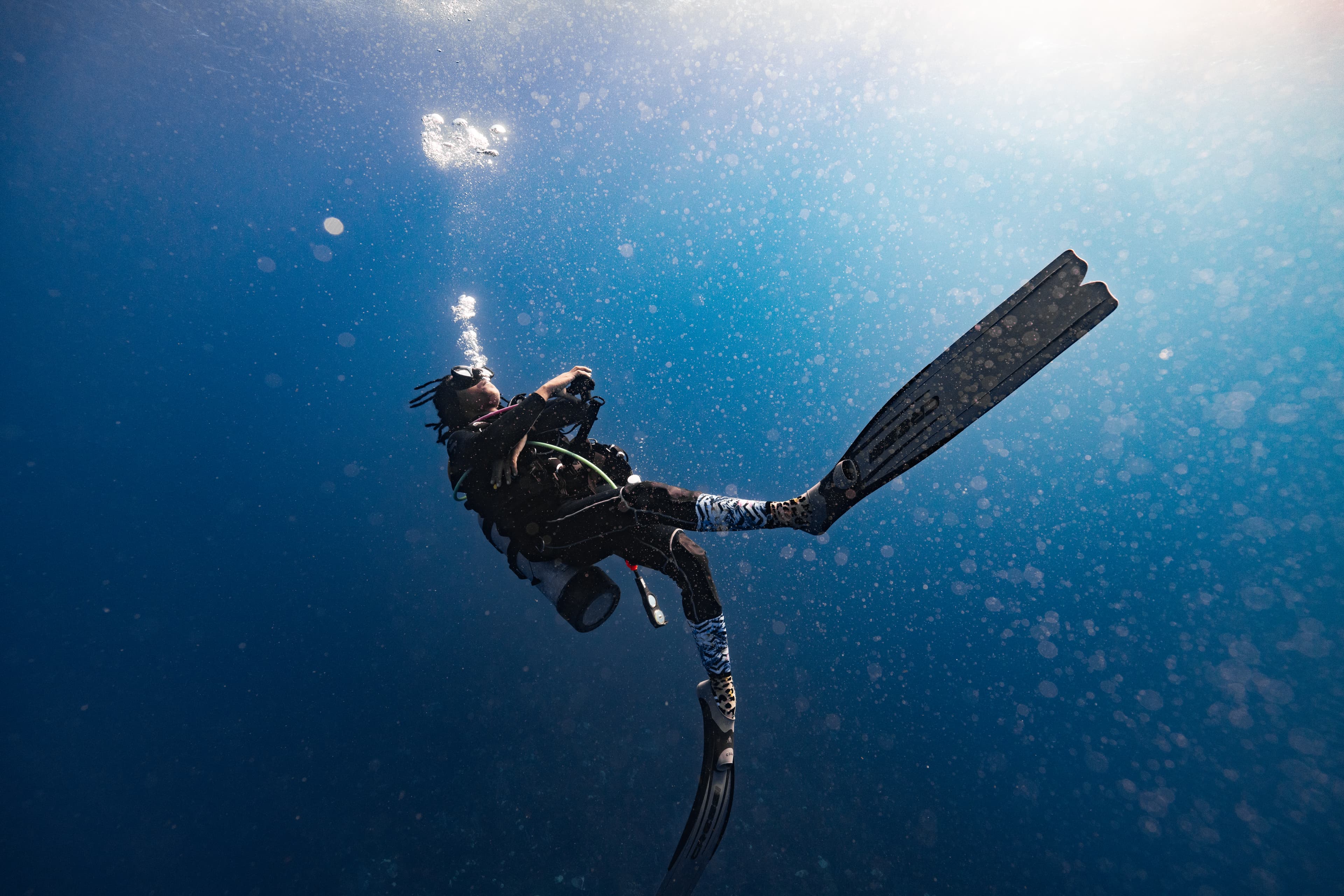A scuba diver is swimming underwater amidst bubbles and sunlight.