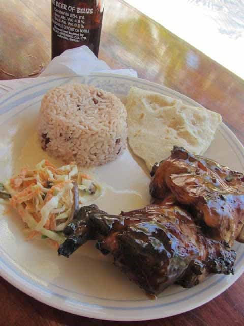 A plate of grilled chicken, rice and beans, a tortilla, coleslaw, and a bottle of beer.