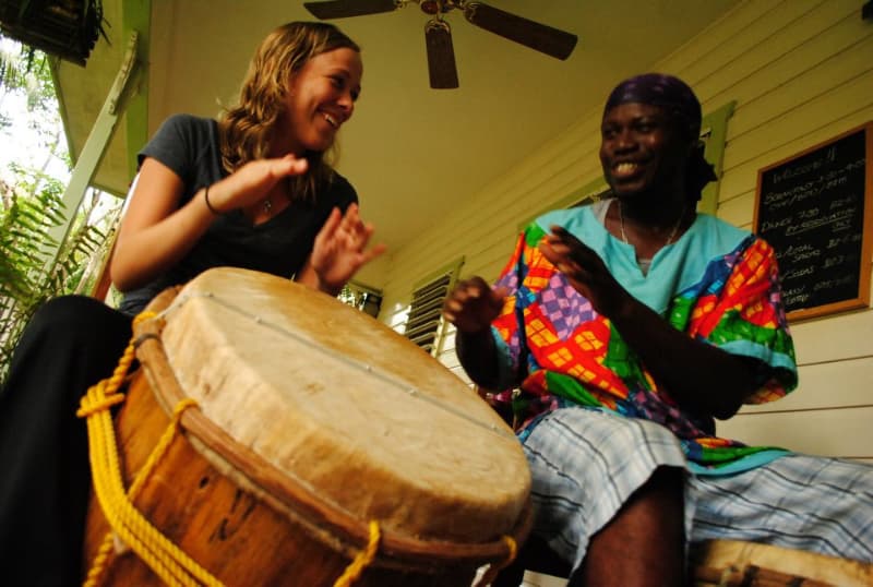 A woman and a man joyfully play a drum together in a vibrant, casual setting.