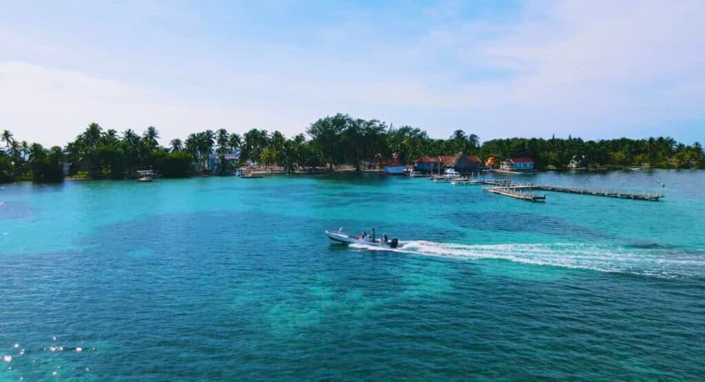 A boat glides through turquoise waters near a lush, green island.