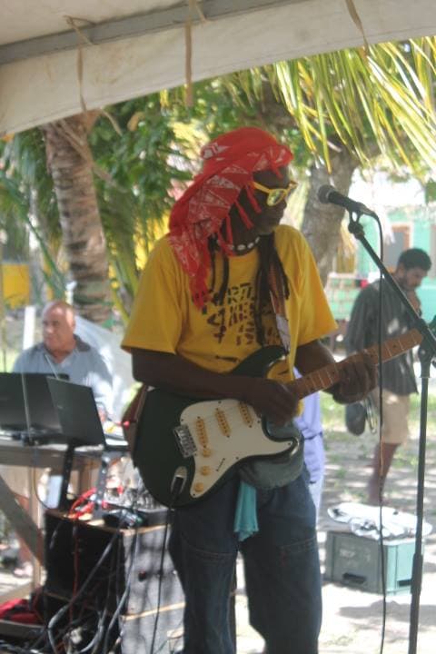 A musician in a yellow shirt and red bandana plays an electric guitar on stage.
