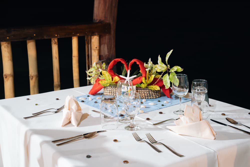 A beautifully set dining table with decorative elements, including a floral centerpiece, glassware, and folded napkins, against a dark background.