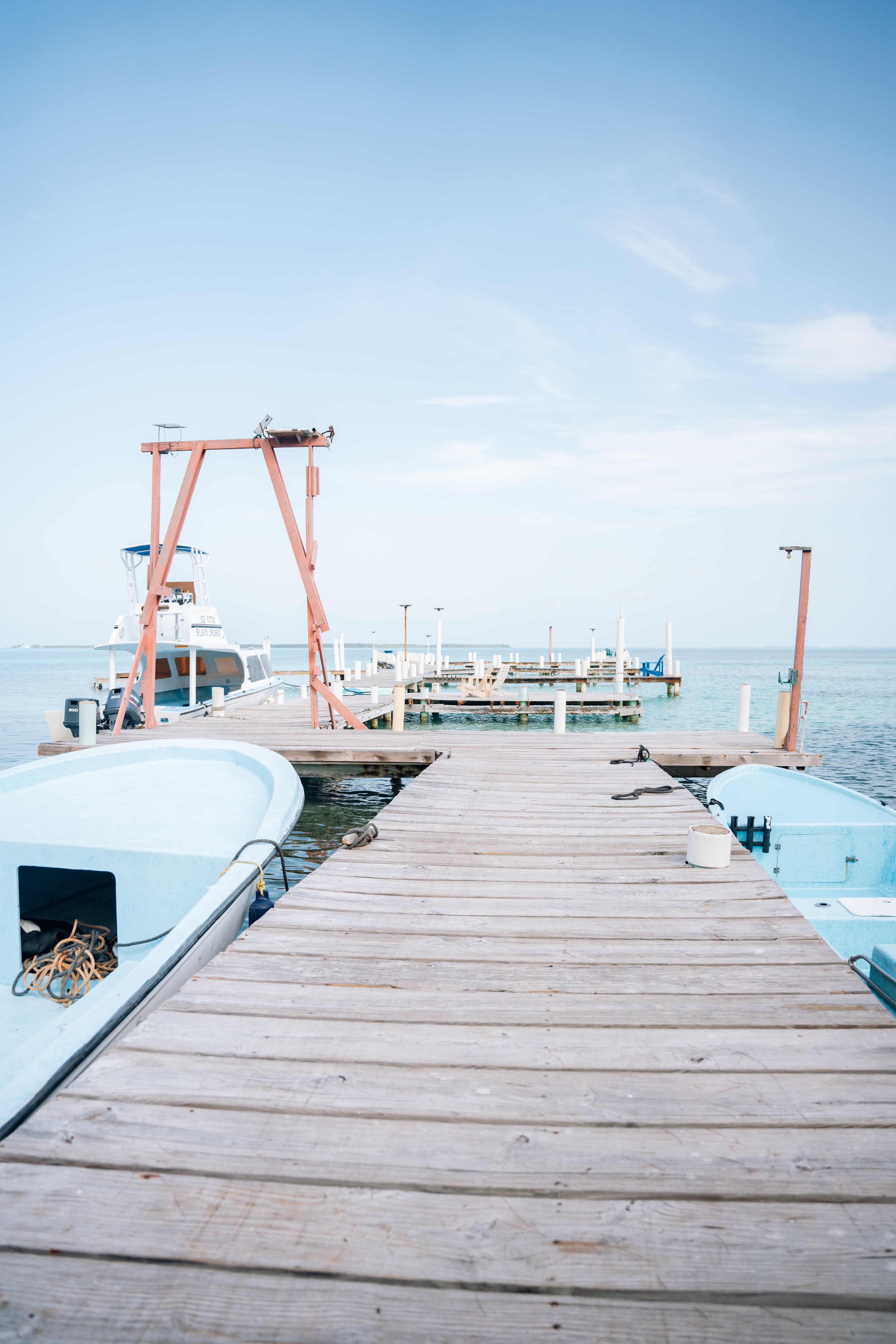 Wooden dock extending toward calm waters and boats under a clear sky.