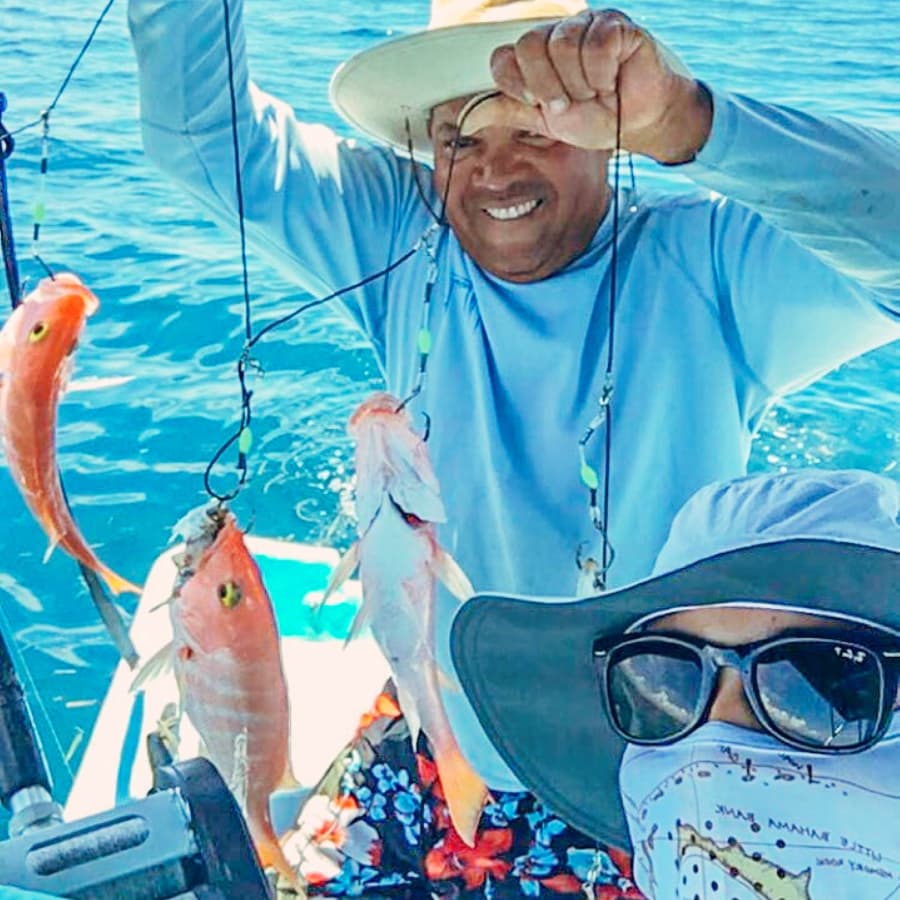 A smiling fisherman holds up several caught fish while posing on a boat.