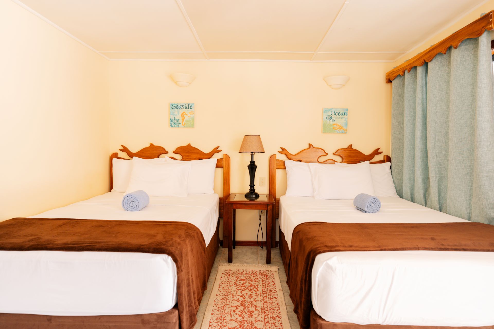 A cozy bedroom with two twin beds, a lamp, and light blue curtains.