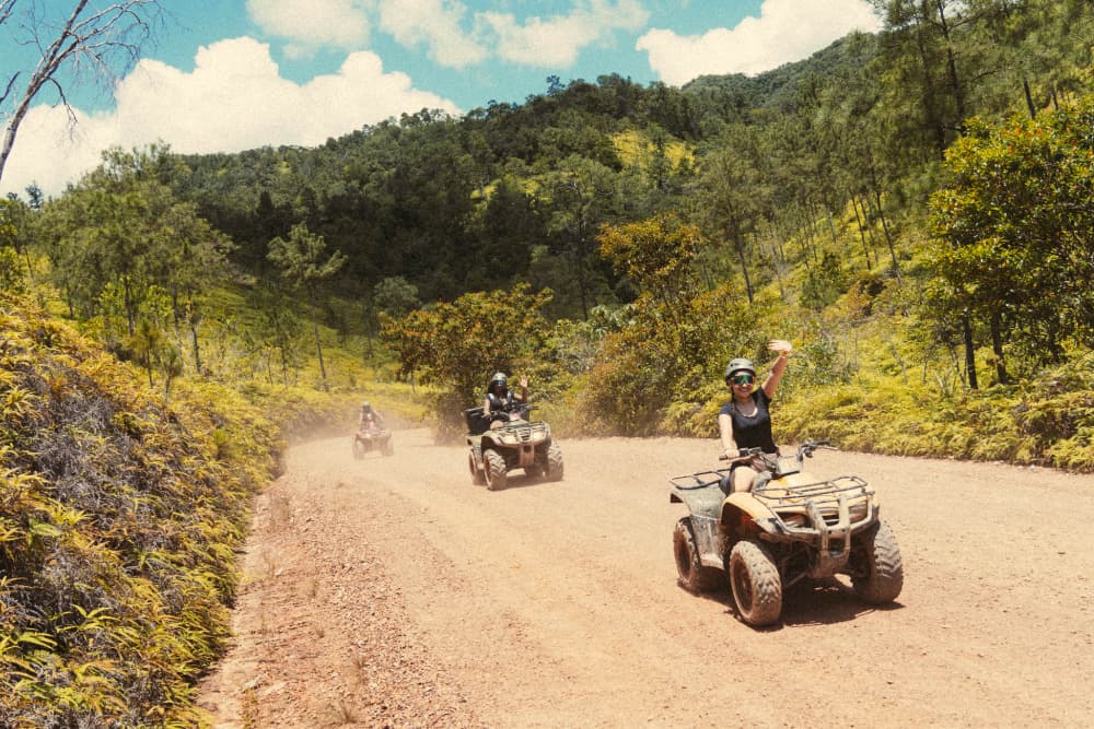 A group of four people rides ATVs on a dirt trail surrounded by lush greenery.