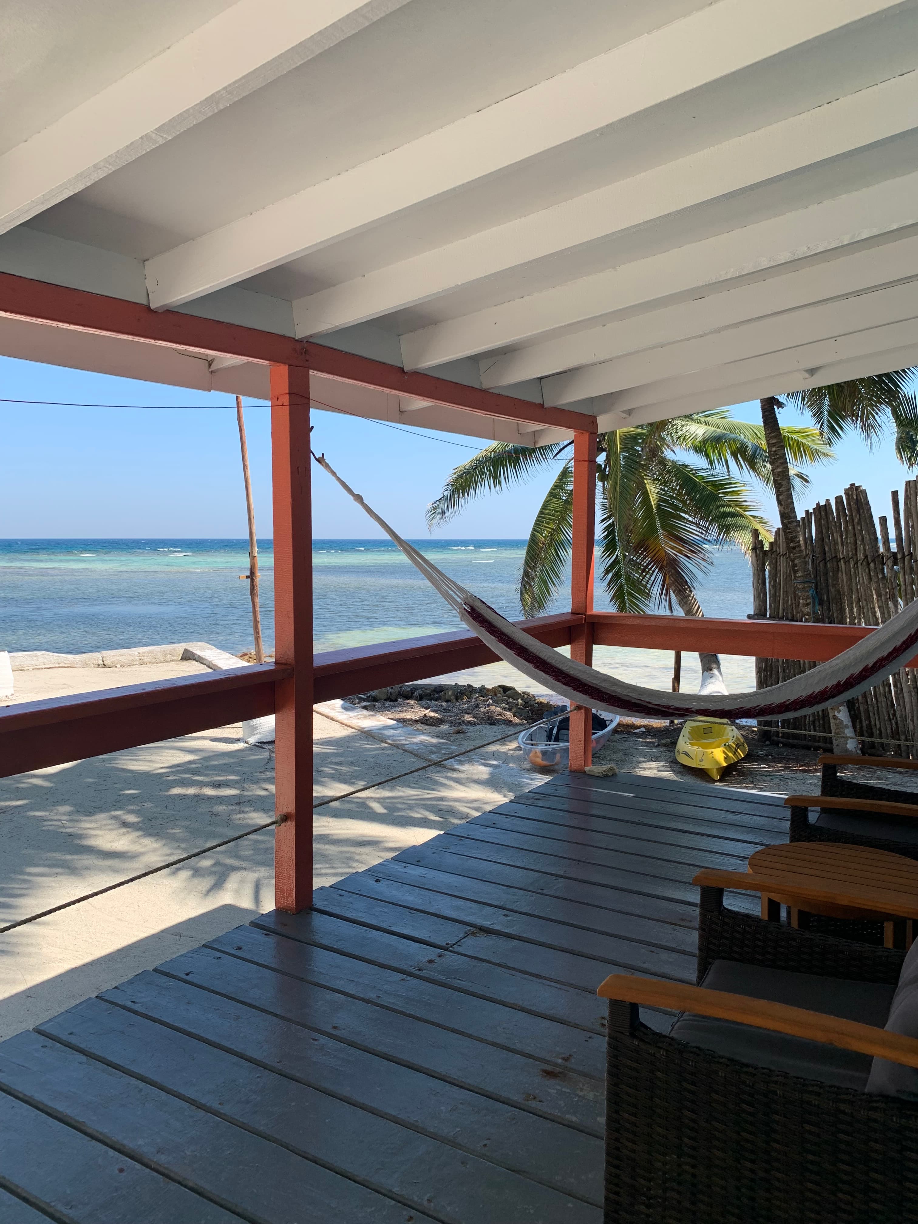 A cozy porch overlooking the ocean with a hammock and palm trees in view.