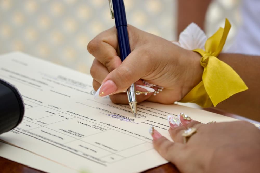 A hand with decorated nails signs a document with a pen.