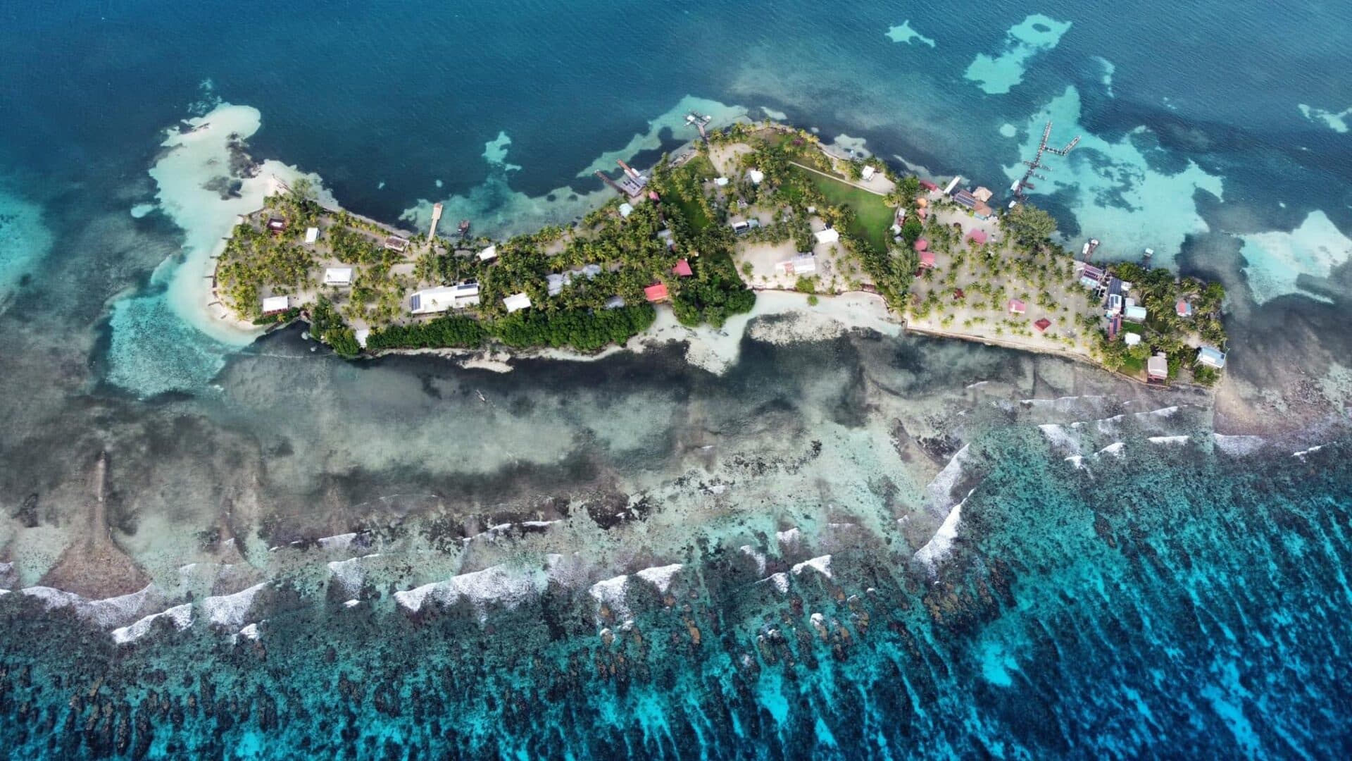 Aerial view of a lush, tropical island surrounded by clear blue waters and coral reefs.
