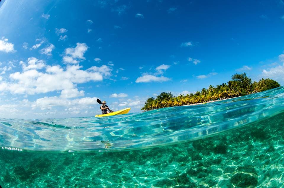 A person kayaking in clear blue water with a tropical island in the background.