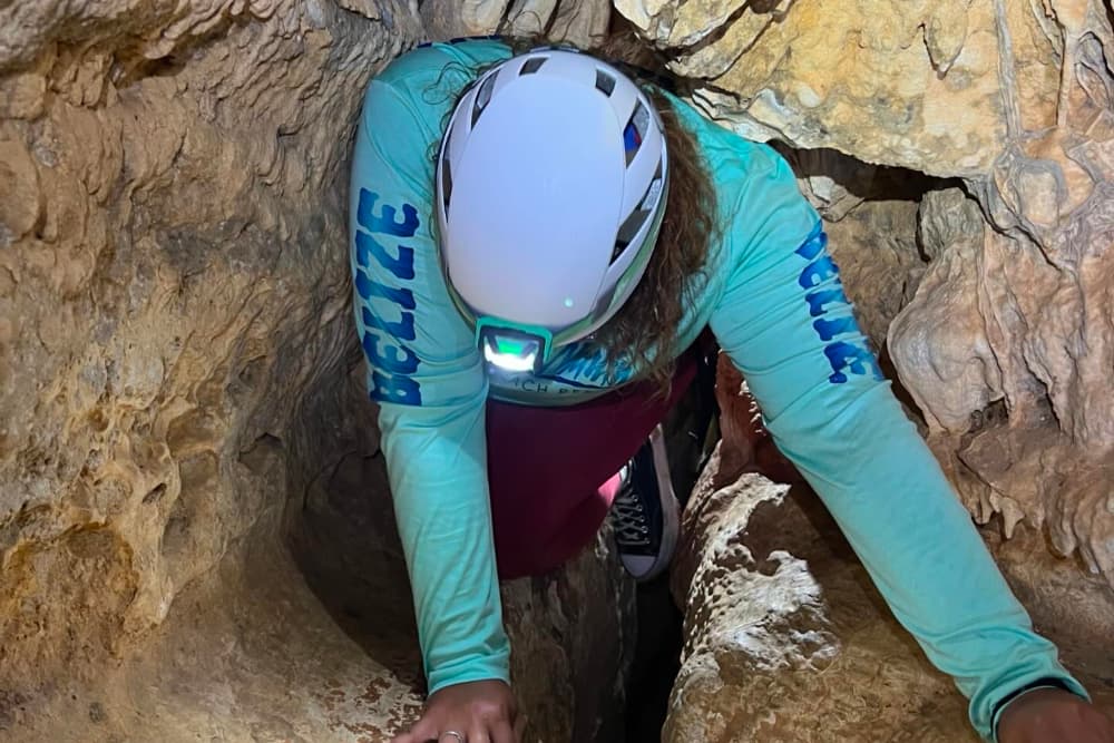 A person wearing a helmet crawls through a narrow cave.