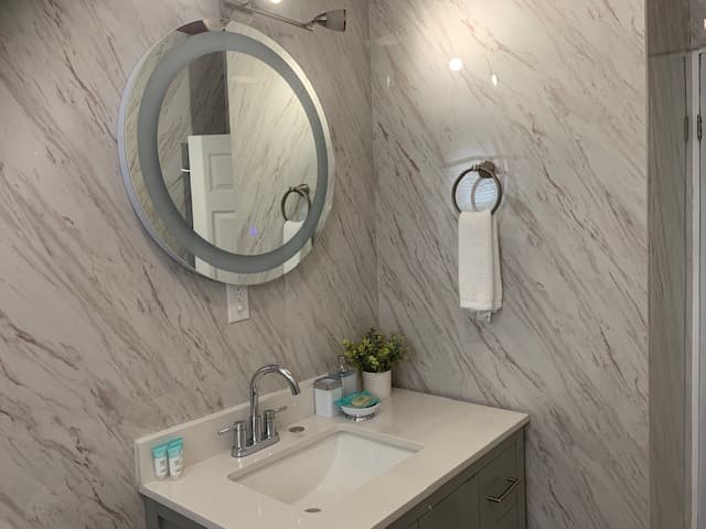 A modern bathroom featuring a marble wall, circular mirror, sink, and decorative plants.