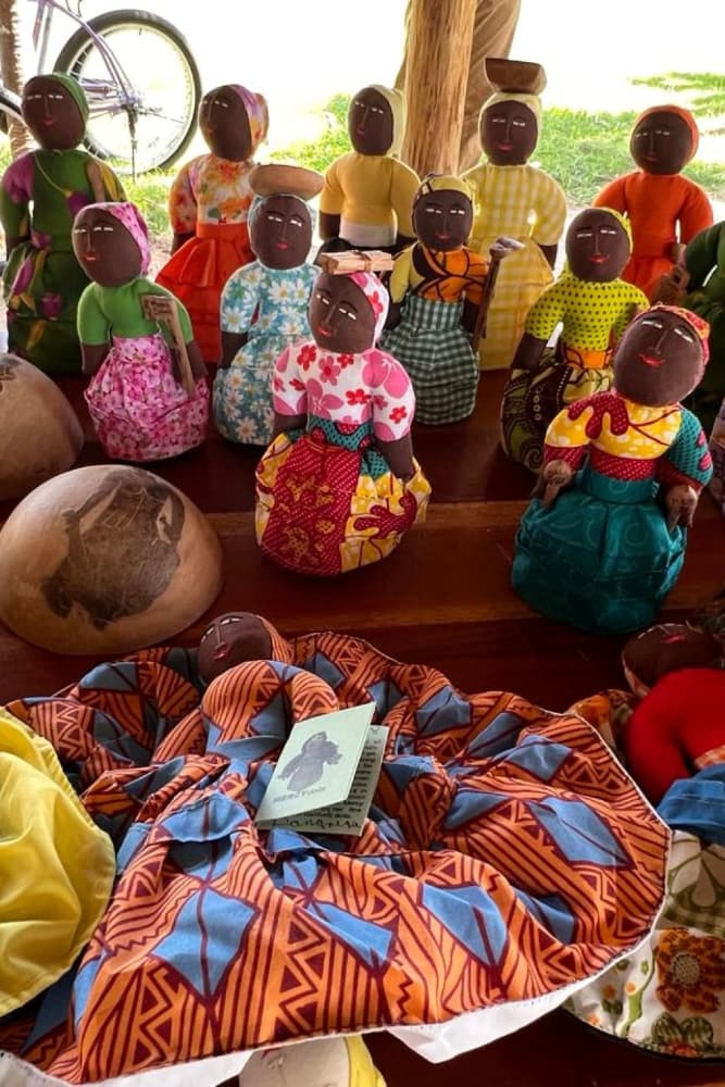 A collection of colorful handmade dolls displayed alongside patterned fabric and pottery.