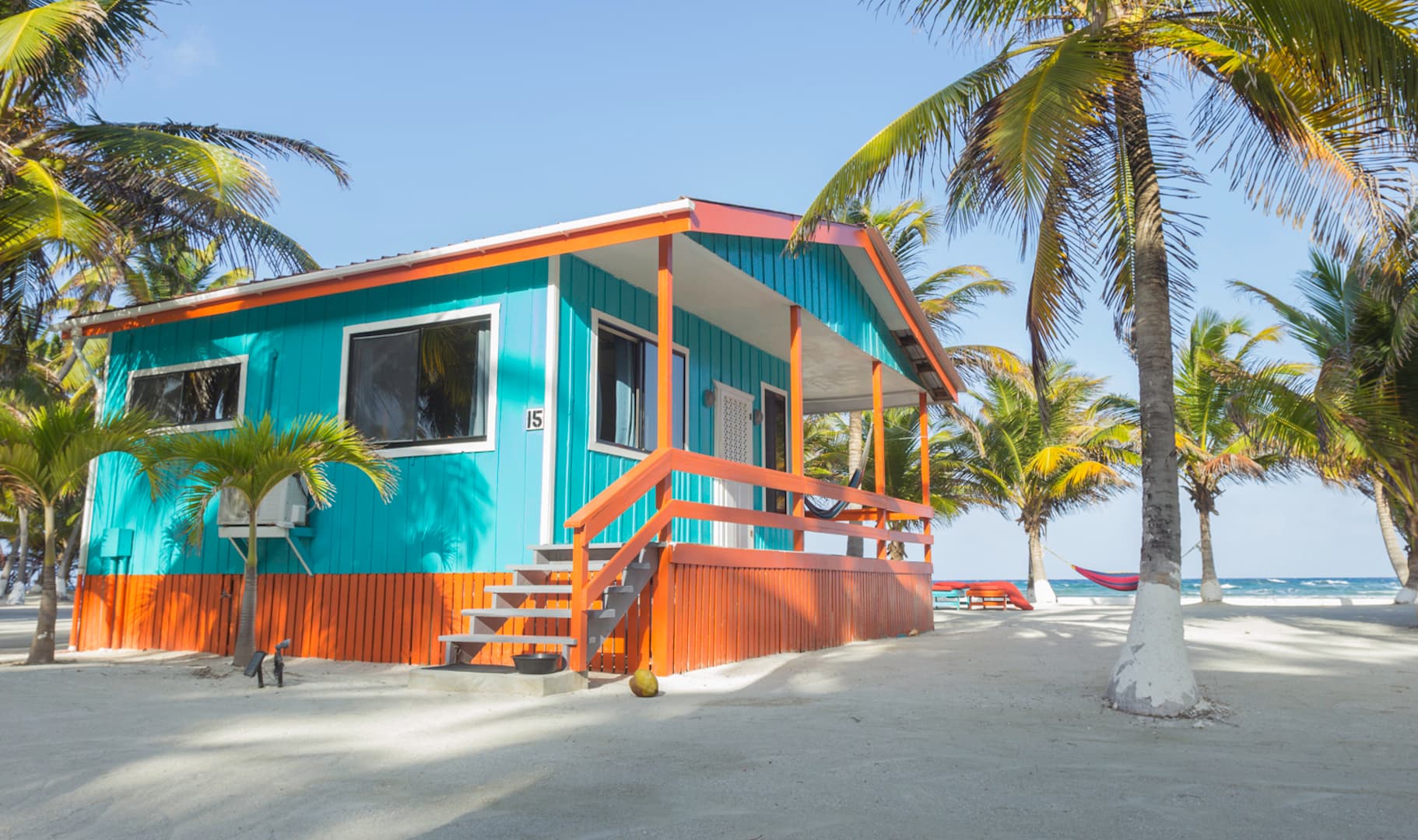 A colorful beachfront cabin surrounded by palm trees and sand.