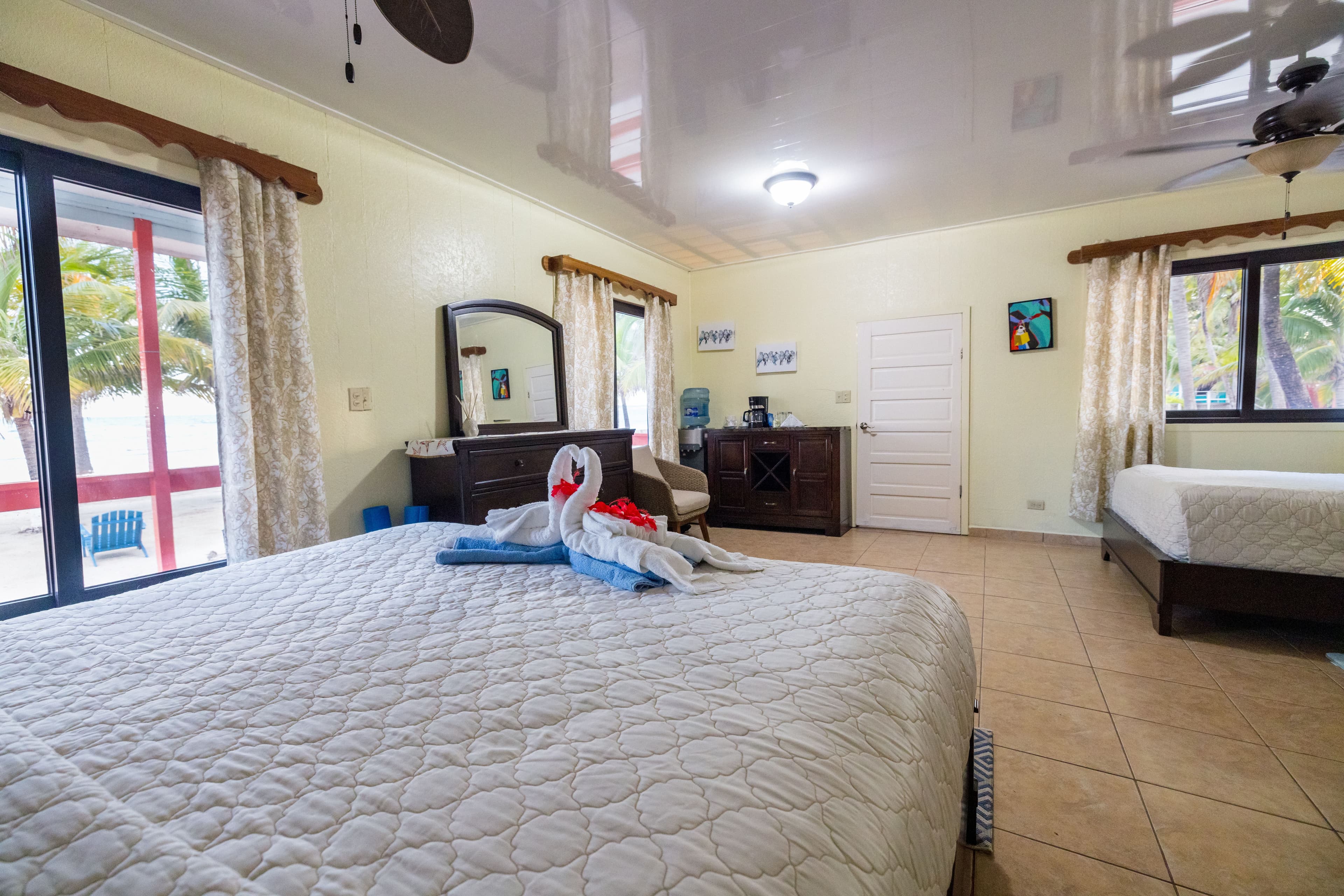 A cozy bedroom featuring a large bed, wooden furniture, and tropical decor.