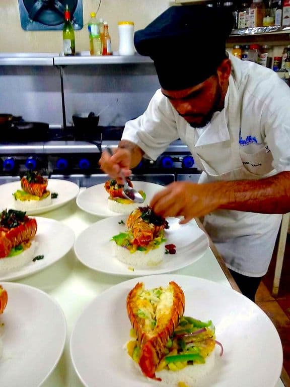 A chef carefully plating lobster over rice and vegetables in a busy kitchen.
