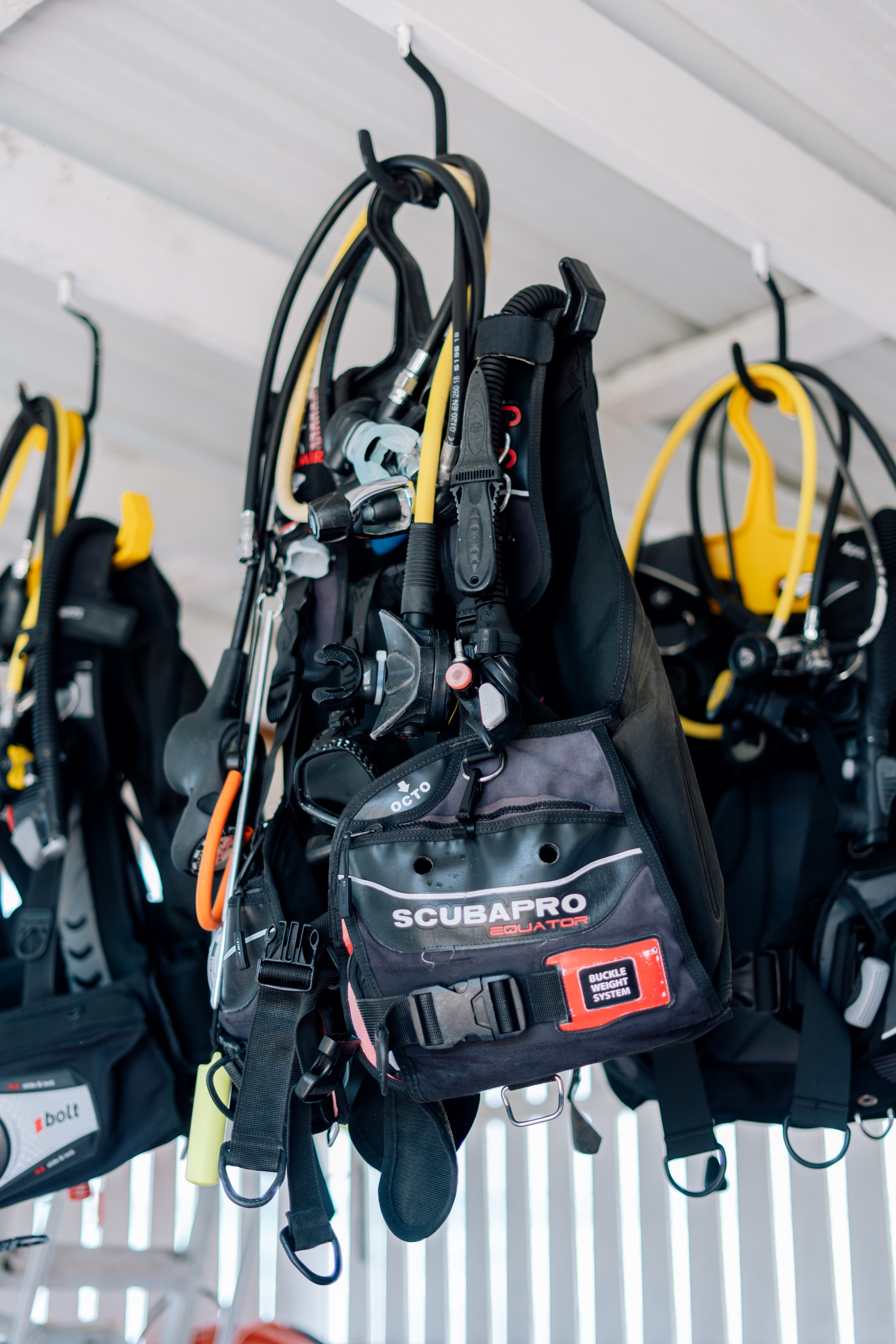 A collection of scuba diving gear hangs from hooks in a well-lit space.