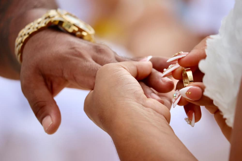 A close-up of two hands exchanging a wedding ring.