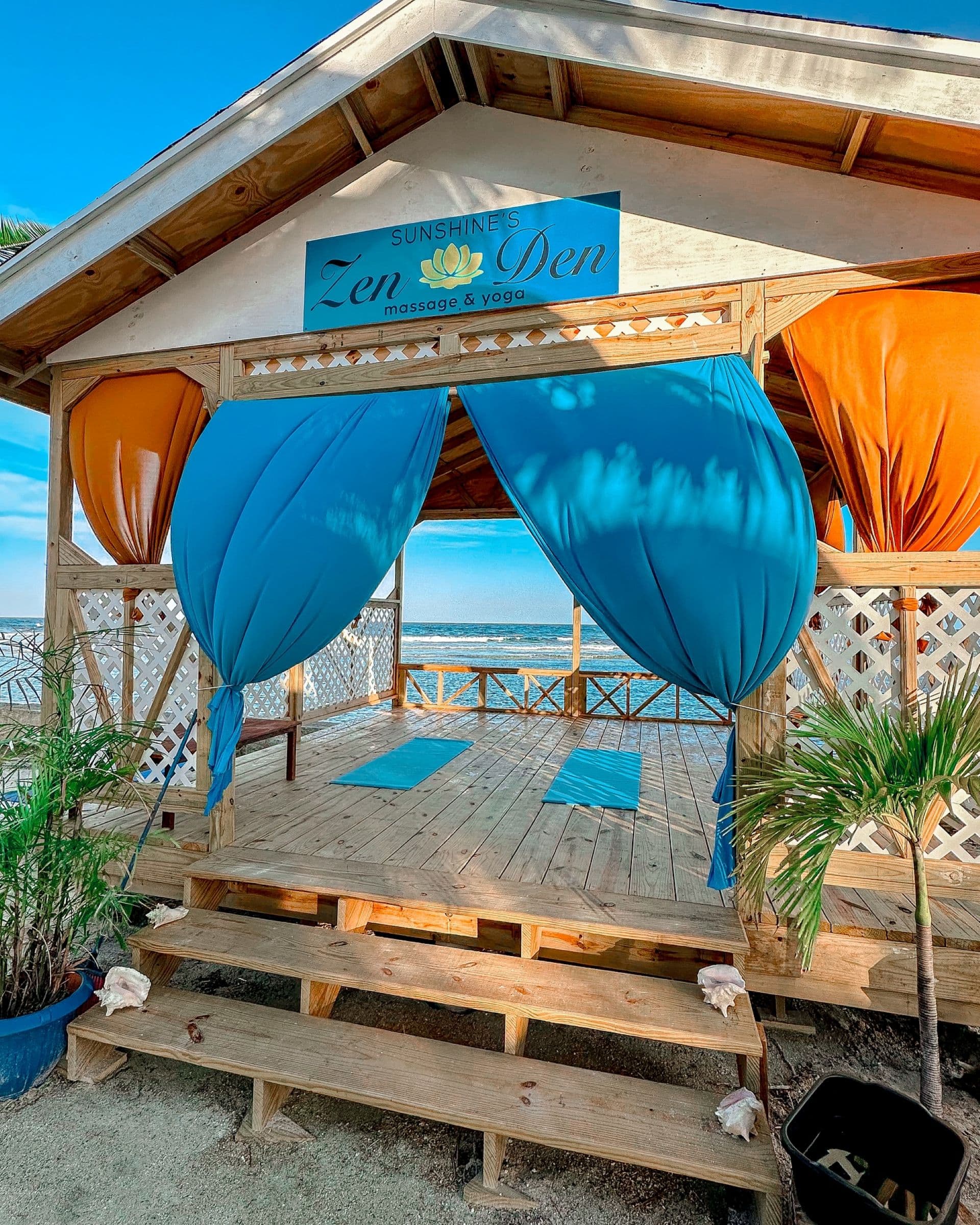 A tranquil seaside massage and yoga pavilion with colorful drapes and wooden deck.