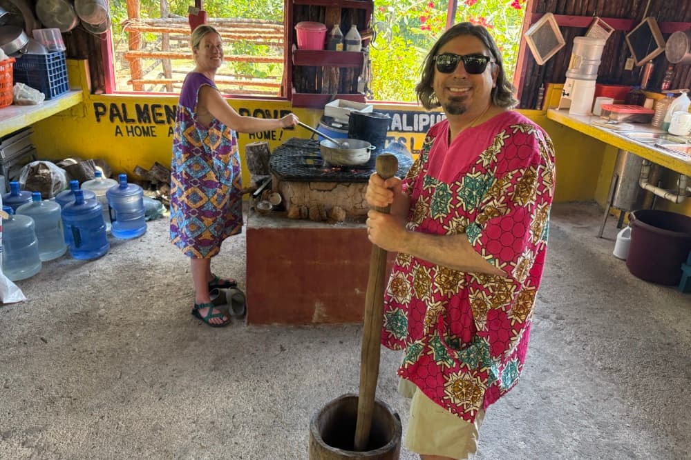 Two people in colorful clothing prepare food in a rustic kitchen.
