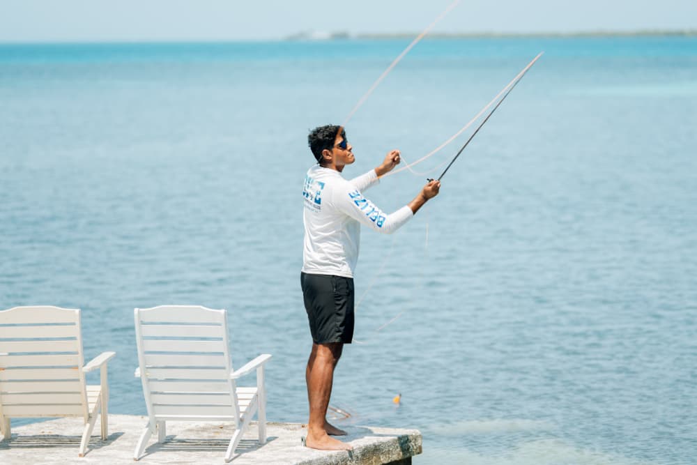 A person stands on a dock casting a fishing line into the water.