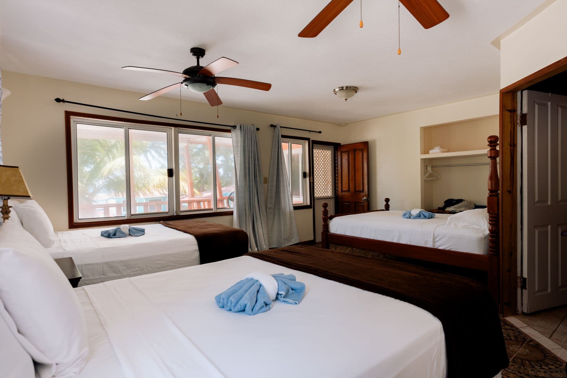 A spacious bedroom featuring two beds, a ceiling fan, and large windows with curtains.