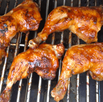 Grilled chicken legs coated in a shiny glaze on a barbecue grill.