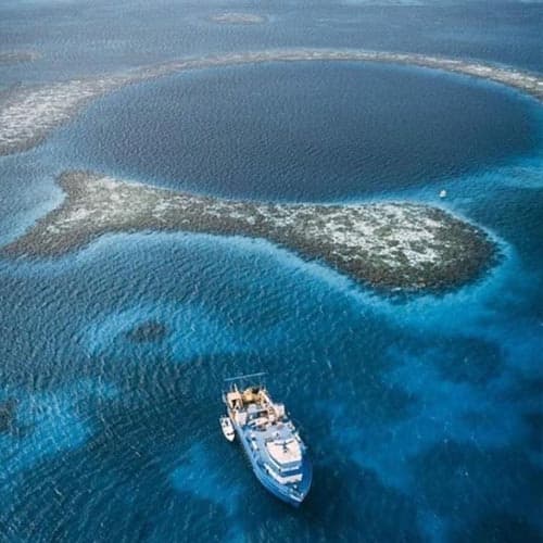 An aerial view of a blue ocean with a circular reef and a research boat.