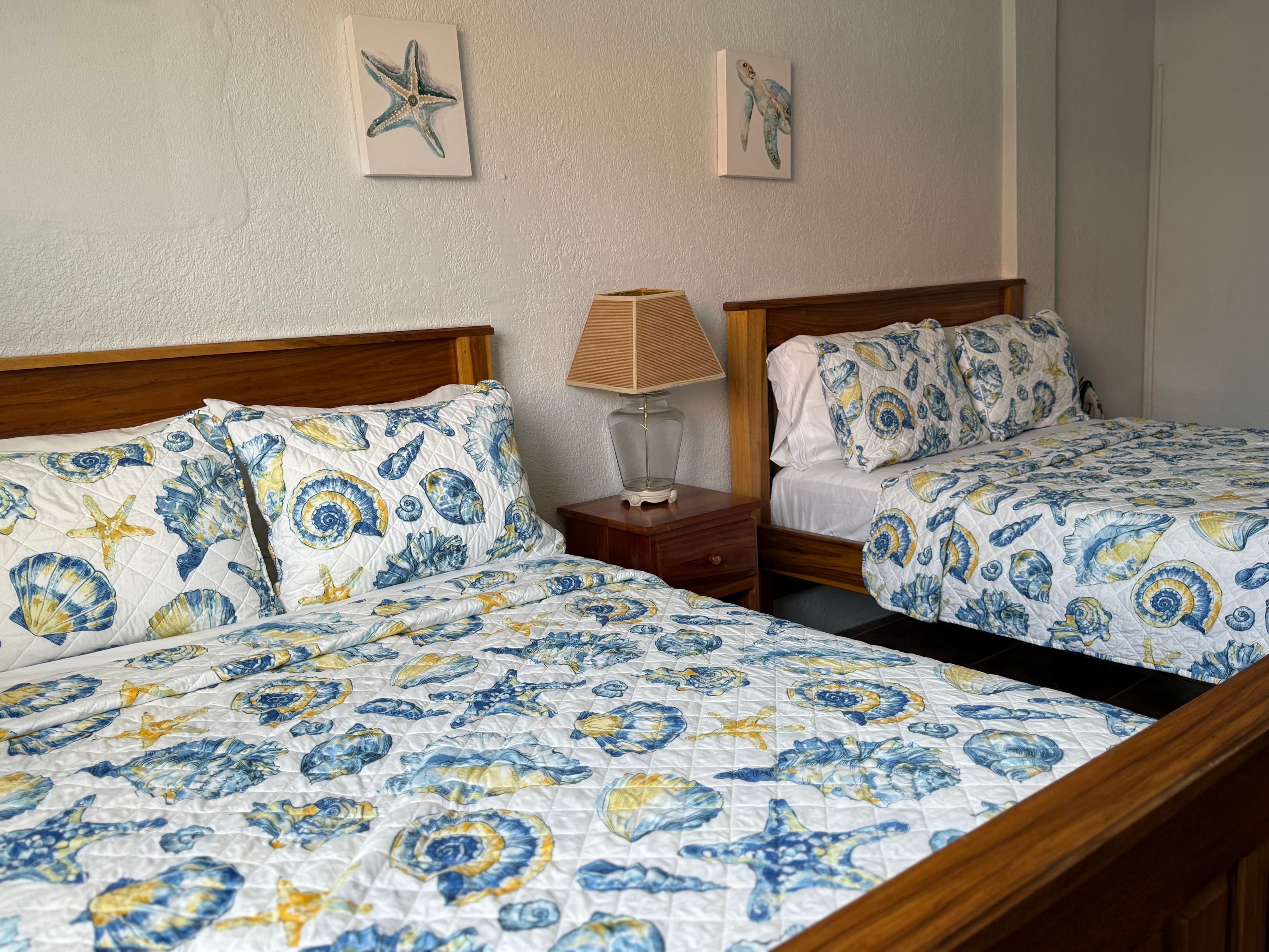 A cozy bedroom featuring two beds with blue and yellow seashell-patterned bedding and beach-themed wall art.