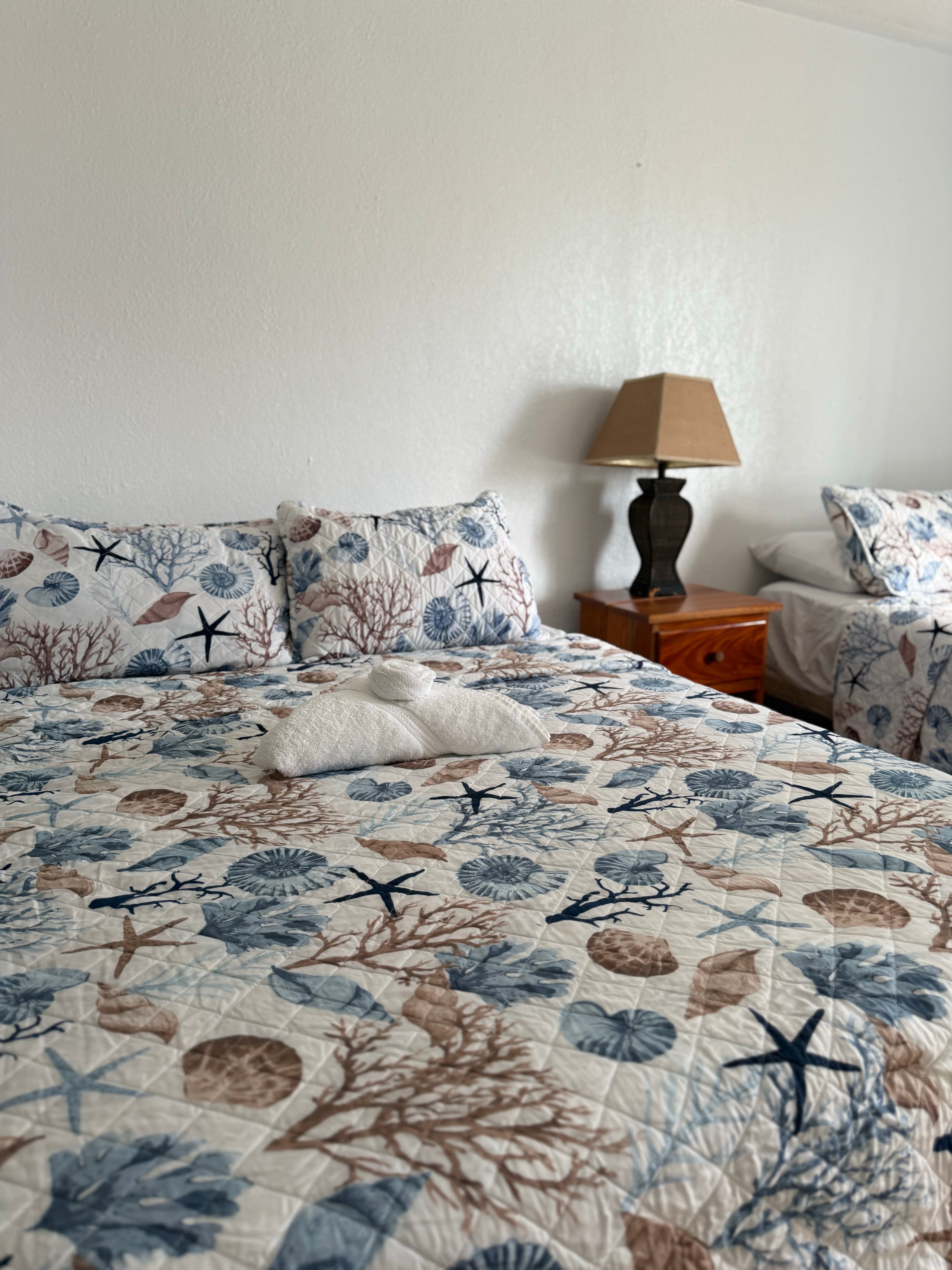 A cozy bedroom with patterned bedding, pillows, and a bedside lamp.