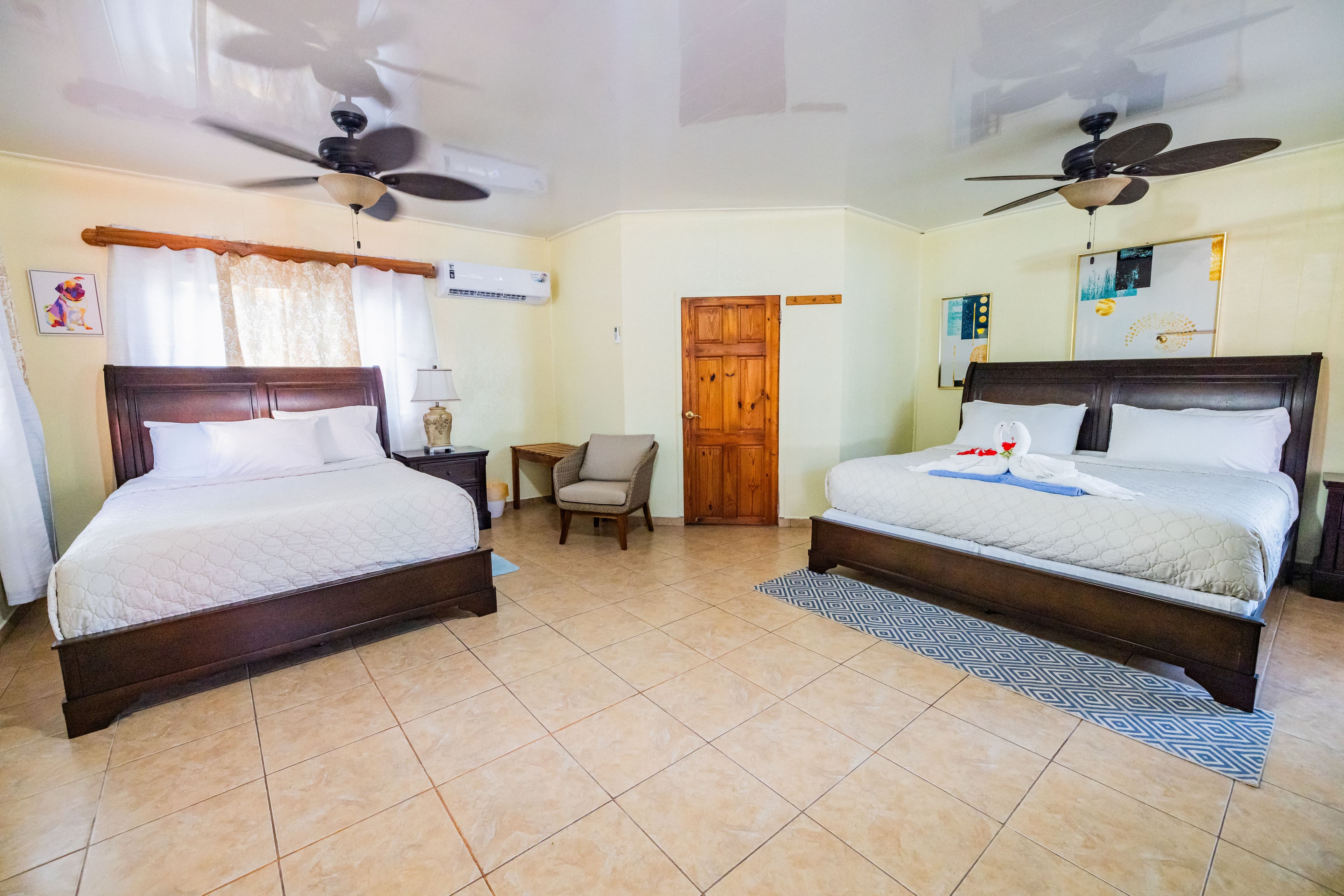 A bright hotel room featuring two large beds, a seating area, and a door.