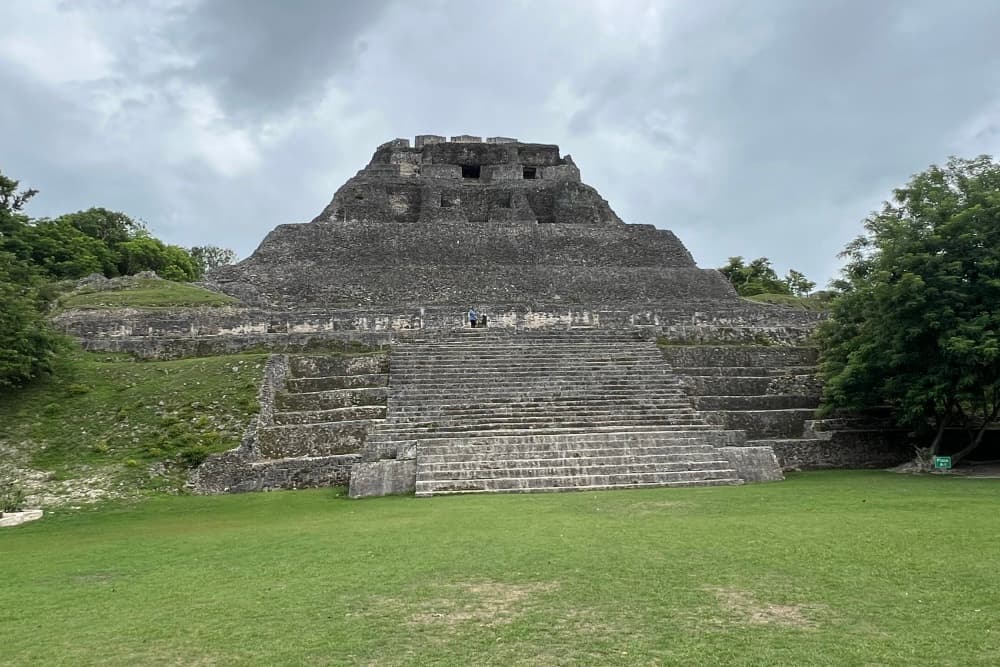 A stone pyramid surrounded by greenery under a cloudy sky.