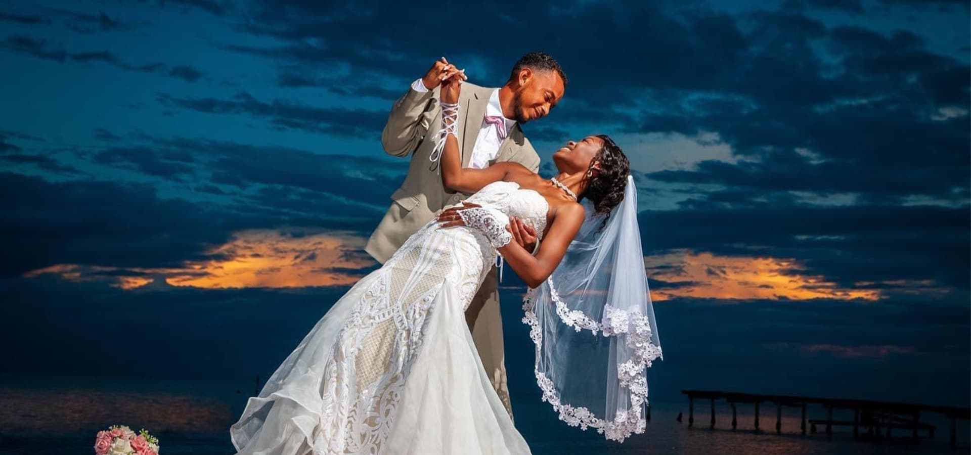 A joyful couple shares a romantic dance at sunset, set against a serene beach backdrop.