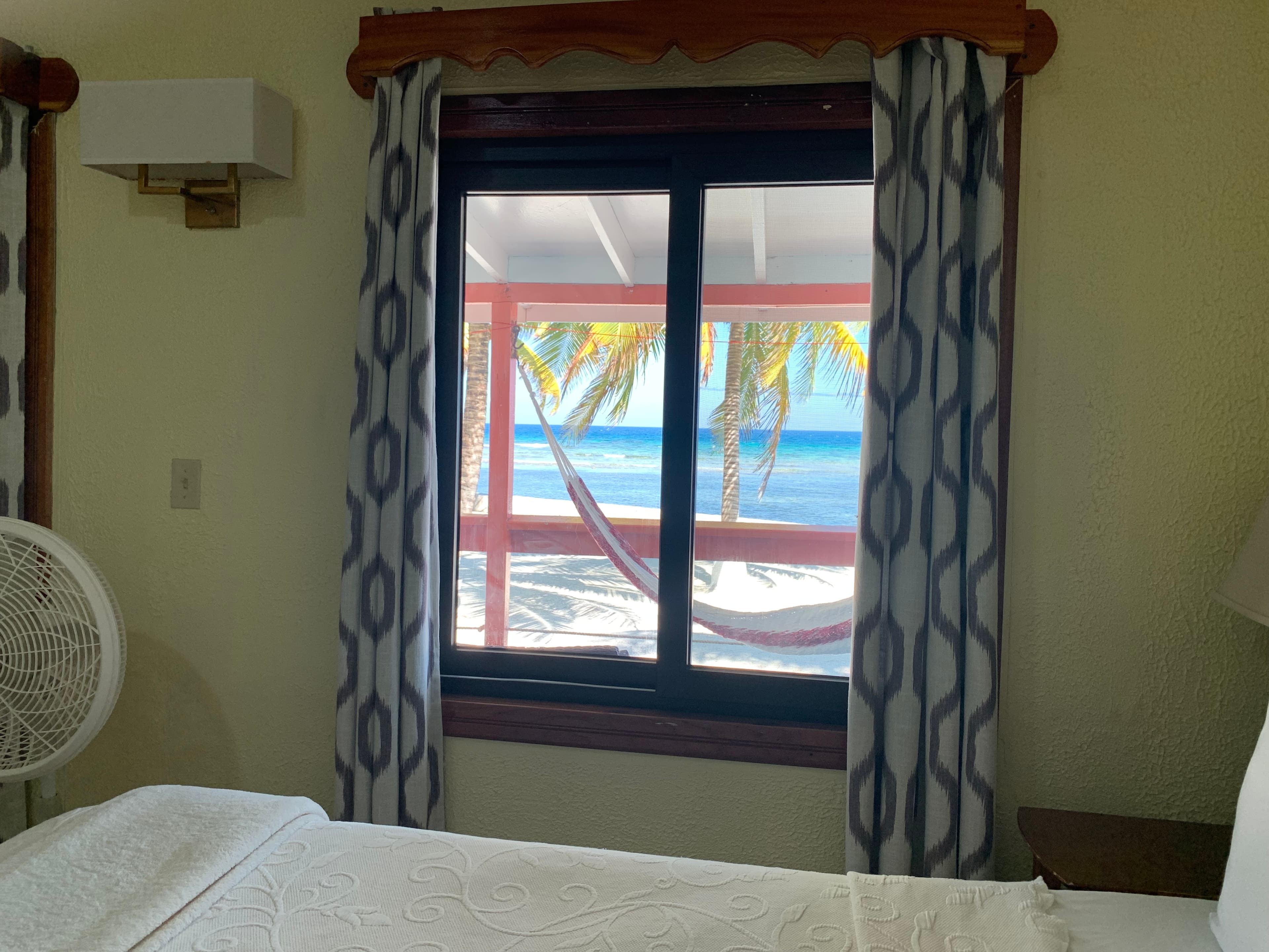 View from a window showing palm trees and a hammock by the beach.